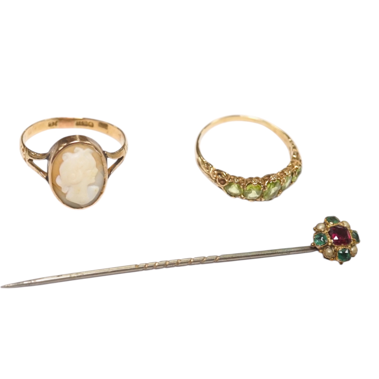 A 9ct and graduated five stone peridot set half hoop ring, size V, a 9ct gold and cameo shell ring and a gem set stickpin. Condition - poor to fair